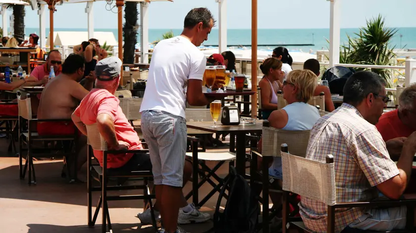 Un lavoratore stagionale mentre serve da bere in un locale in riva al mare