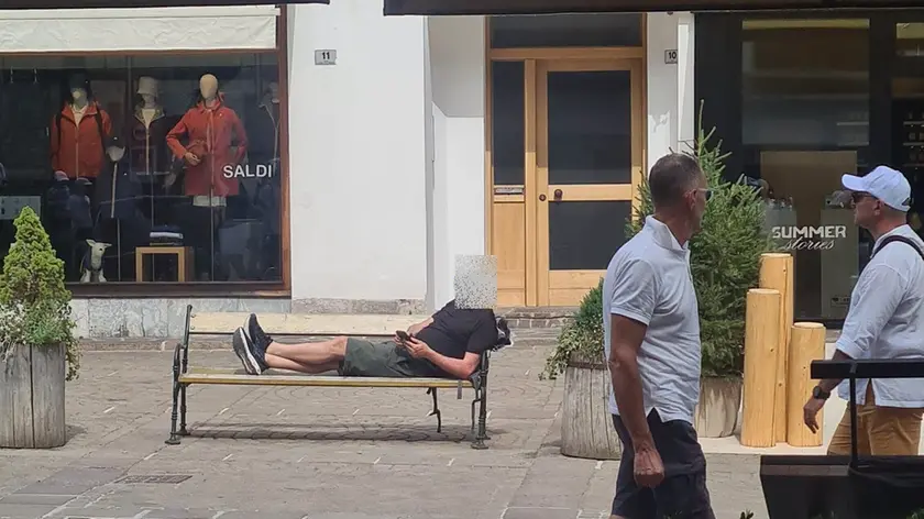 Un turista steso su una panchina a Cortina