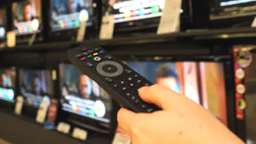 Un utente con il telecomando davanti ai televisori
