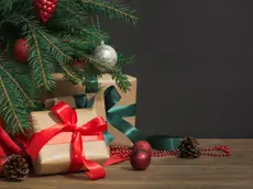 Christmas holiday background. Gifts with a red ribbon, Santa's hat and decor under a Christmas tree on a wooden board. Close up. Copy space on chalkboard.