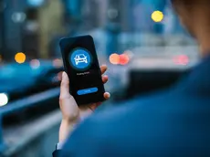 Over the shoulder view of young Asian woman arranging a taxi service with mobile app on smartphone in city street in the evening, with illuminated city scene in background. Lifestyle and transportation technology. Convenience and trustworthy car service