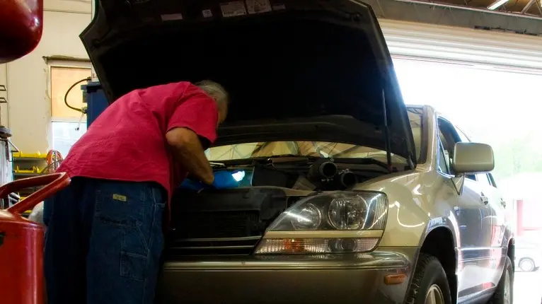 Franklin, North Carolina, USA --- Mechanic working on car, leaning in under open hood. --- Image by © Third Eye Images/Corbis